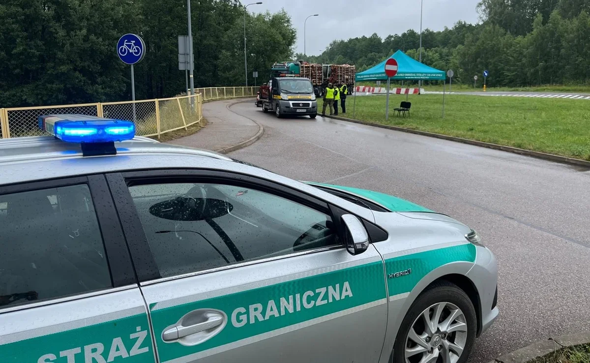 Samochód Straży Granicznej z włączonymi niebieskimi światłami stoi na drodze w pobliżu punktu kontrolnego, gdzie funkcjonariusze zatrzymali ciężarówkę przewożąc