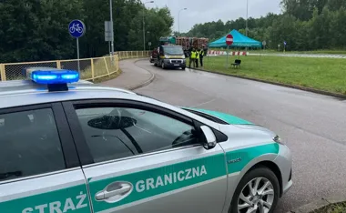 Samochód Straży Granicznej z włączonymi niebieskimi światłami stoi na drodze w pobliżu punktu kontrolnego, gdzie funkcjonariusze zatrzymali ciężarówkę przewożąc